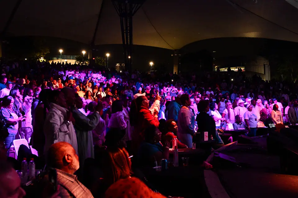 Thousands of concertgoers on their feet under purple stage light at the Aretha Franklin Amphitheatre