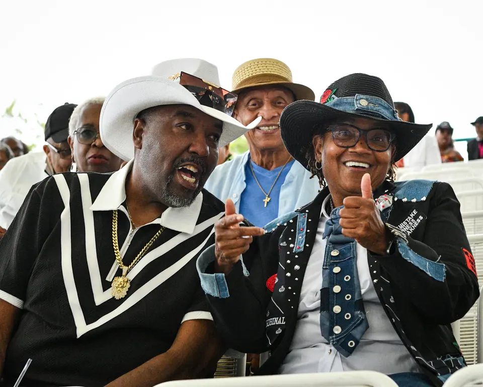 Two guests in statement hats laugh together in their seats